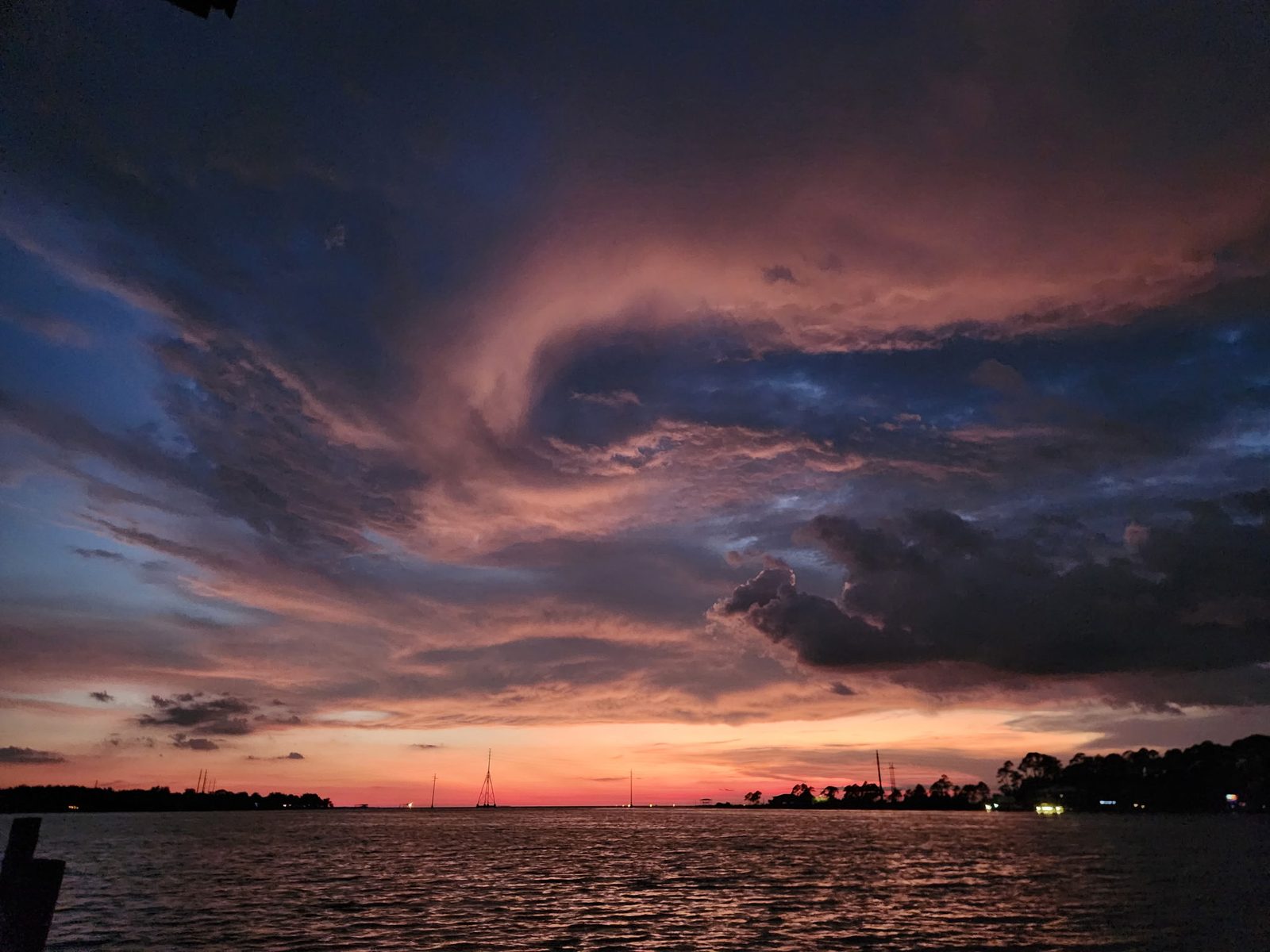 Swirling pink and dark blue storm clouds at dusk over open water and a low far shore.