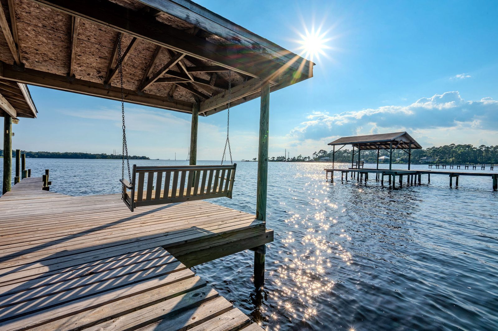 A wooden swing hanging on chains under the roof of the covered dock, over open water in afternoon sun.